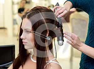 Hair stylist making ringlets to brunette woman. Hairdresser work