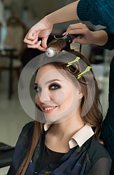 Hair stylist making ringlets to brunette woman. Hairdresser work