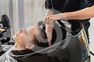 Hair stylist washing hair of yong blonde girl in hair salon before haircut