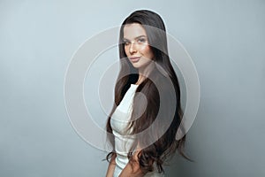 Haircare concept. Beautiful brunette woman with smooth straight healthy silky hair posing on grey background portrait