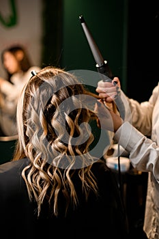 hairdo making process, stylist curls long female hair with modern clipless curling iron