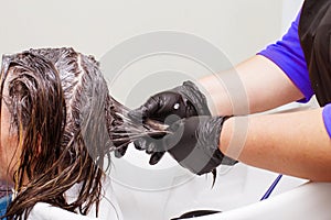 The hairdresser in black gloves paints a brunette woman`s hair in the beauty salon