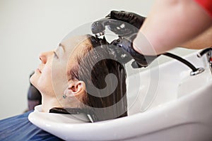 The hairdresser in black gloves washing brunette woman& x27;s hair in the beauty salon.