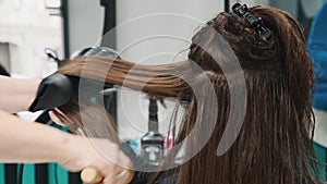 Hairdresser blow dry hair in beauty salon with hair dryer and comb. Woman with straight silky shiny long brown hair