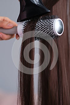 Hairdresser blow drying her hair. Blow dryer close up. Drying long brown hair with hair dryer and round brush.