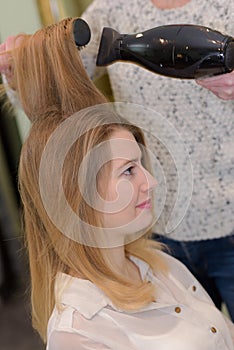 Hairdresser blow drying long brown hair using round brush