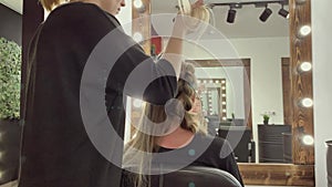 Hairdresser braiding woman`s hair in hairdressing salon.