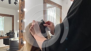 Hairdresser braiding woman`s hair in hairdressing salon.