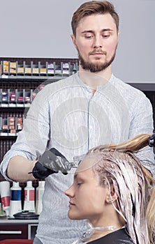 A hairdresser coloring hair of a blonde female client