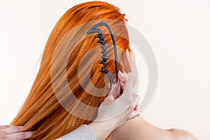 Hairdresser is combing her long red hair of beautiful woman in the beauty salon. Professional hair care and creating hairstyles