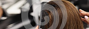 Hairdresser combing long hair of client in beauty salon closeup