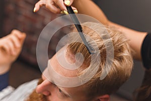 Hairdresser combs hair of handsome client before haircut in barbershop