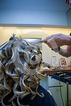 Hairdresser curling a blonde woman`s hair
