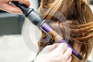 Hairdresser with curling iron curls hair