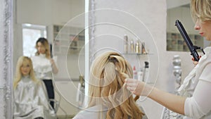 Hairdresser curls blonde hair with curling iron