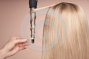 The hairdresser curls long hair with a Curling iron