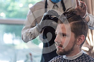 A hairdresser cuts a bearded young guy with a hair trimmer, combing the hair on his head. Work of the master in men`s haircut in