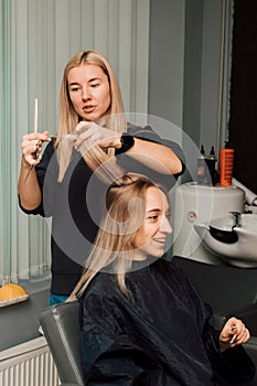 A hairdresser cuts a blonde& x27;s hair in a beauty salon. Women& x27;s haircut