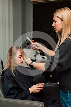 A hairdresser cuts a blonde& x27;s hair in a beauty salon. Women& x27;s haircut