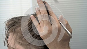 Hairdresser cuts hair on the temple and nape to client in a salon. Man sitting in hairdressers armchair while shearing