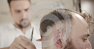 Hairdresser cuts hair to man in barbershop, getting a modern haircut