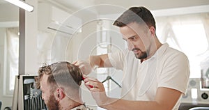 Hairdresser cuts hair to man in barbershop, getting a modern haircut