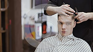 Hairdresser cuts hair of young man in barbershop