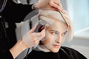 Hairdresser cuts woman client with trimmer. A short haircut, shaved temple and a drawing on the hair.