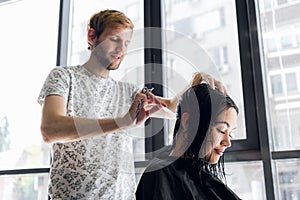 Hairdresser cutting client`s hair in salon with scissors closeup. Using a comb