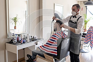 Hairdresser cutting hair at barber shop wearing mask