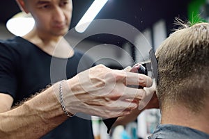 Hairdresser is cutting hair of handsome bearded mature man in salon. Stylist making hairstyle with electric shaver for person in