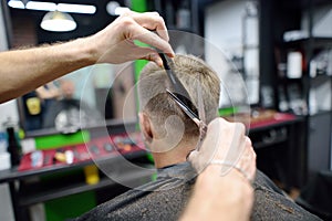 Hairdresser is cutting hair of handsome bearded mature man in salon. Stylist making hairstyle for person in barbershop. Services