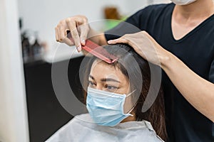 Hairdresser cutting the hair to female client, people must be wering medical mask to protection coronavirus covid-19 pandemic.