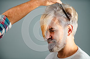 Hairdresser cutting male hair, closeup. Hairdresser does hair with black comb of handsome client in professional