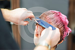 Hairdresser cutting short pink hair in beauty salon