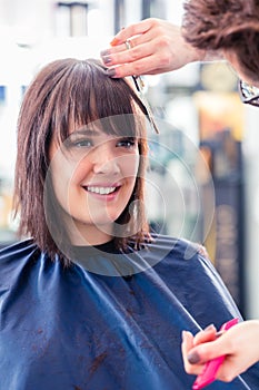 Hairdresser cutting woman hair in shop