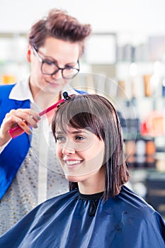 Hairdresser cutting woman hair in shop