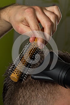 Hairdresser does hair with brush and hairdryer of client in professional hairdressing salon