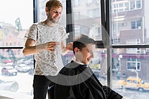 Hairdresser does hair with comb of handsome satisfied client in professional hairdressing salon