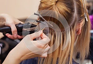 The hairdresser does hair extensions to a young girl, a blonde in a beauty salon.