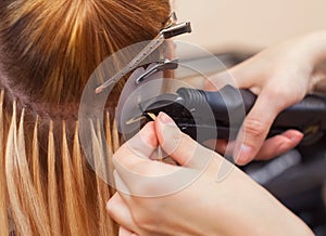 The hairdresser does hair extensions to a young girl, a blonde in a beauty salon. photo