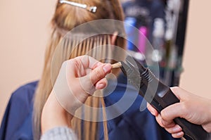 The hairdresser does hair extensions to a young girl, a blonde in a beauty salon photo