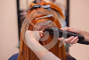 The hairdresser does hair extensions to a young, red-haired girl