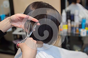 The hairdresser does a haircut with hot scissors of hair to a young girl, a brunette