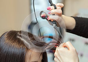 The hairdresser does a haircut with hot scissors of hair to a young girl, a brunette in a beauty salon.Professional hair care and