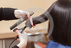 The hairdresser does a haircut with hot scissors of hair to a young girl, a brunette
