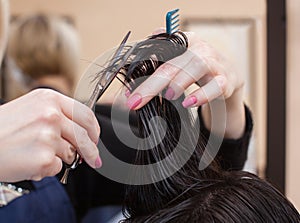 The hairdresser does a haircut with hot scissors of hair to a young girl, a brunette