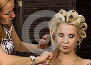 Hairdresser does hairstyle for luxurious blond woman. coiffure in the form of big curl. Concept wedding hairstyle