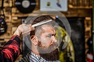 Hairdresser does styling with a comb in barbershop. Bearded man in barber shop. Work in the barber shop. Man hairstylist