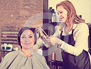 Hairdresser does to woman haircut with use of scissors and hairbrushes